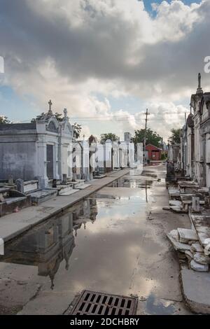 Ein überfluteter Weg, der von großen Bäumen beschattet und von historischen Grabsteinen und Gräbern umgeben ist. lafayette Friedhof New Orleans Louisiana Stockfoto