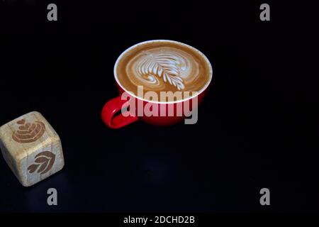 Latte Art Würfel und Kaffee mit Latte Art in roter Tasse und schwarzem Hintergrund. Stockfoto