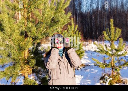 Neues Jahr 2021 und weihnachtskonzept. Junge Frau in Strickmütze und Schal, die im Winter durch ein Fernglas mit der Nummer 2021 in Okularen schaut Stockfoto