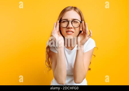 Ein Mädchen in einem weißen T-Shirt, mit schlechtem Augenlicht trägt eine Brille, schaut zuckend und versucht herauszufinden, was auf einem gelben Hintergrund geschrieben ist Stockfoto