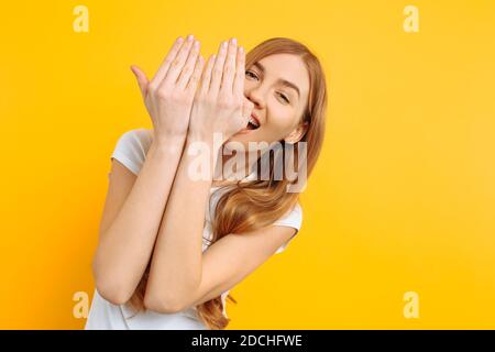 Schönes Mädchen schließt ihre Augen mit ihren Händen, auf einem gelben Hintergrund Stockfoto