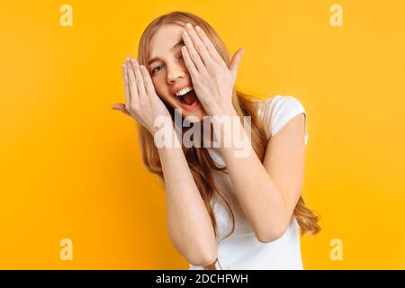 Schönes Mädchen schließt ihre Augen mit ihren Händen, auf einem gelben Hintergrund Stockfoto