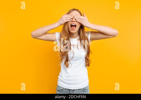 Schönes Mädchen schließt ihre Augen mit ihren Händen, auf einem gelben Hintergrund Stockfoto