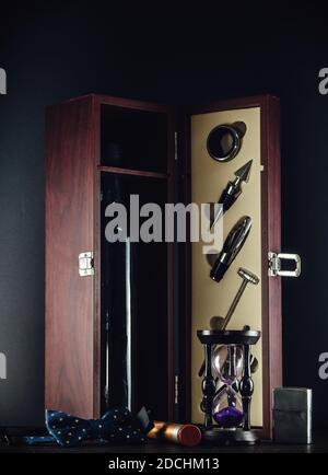 Elegante Weinkiste aus Holz mit fünf Zubehörteilen Geschenkset, altem Feuerzeug, Fliege und Sandglas auf dem Holztisch. Vertikales Bild, schwarzer Hintergrund. Stockfoto