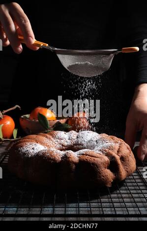 Frau Hand bestreuen Puderzucker über frischen gebundenem Kuchen. Dunkler Hintergrund. Stockfoto