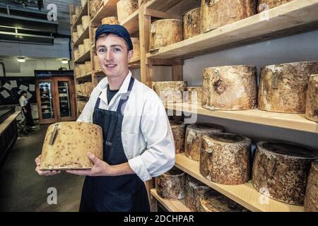 Junger Mann, der einen großen Käse in der Neal s Yard Dairy auf dem Borough Market in Southwark, London, England, hält. Stockfoto