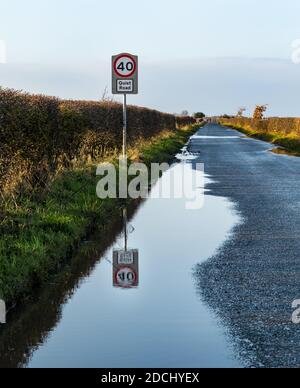 40 mph Geschwindigkeitsbegrenzungsschild auf Landstraße als ruhige Straße mit Reflexion in Pfütze, East Lothian, Schottland, Großbritannien benannt Stockfoto