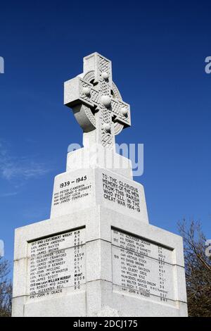 Ballantrae, South Ayrshire, Schottland, Großbritannien, Kriegsdenkmal, das Denkmal steht unter den Ruinen der Burg. Es ist ein graues keltisches Granitkreuz mit Radkopf und Bossen, die auf einem niedrigen, verjüngenden Schaft auf einem großen quadratischen Sockel liegen. Die Gedenkfeier und die Namen der Toten sind in Bleischrift auf den Gesichtern des Sockels angebracht. Die Namen der Toten aus dem 1. Weltkrieg werden nach dem Todesjahr aufgelistet, einschließlich der Namen bis 1920. Stockfoto