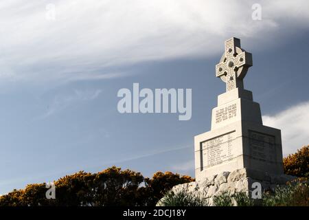 Ballantrae, South Ayrshire, Schottland, Großbritannien, Kriegsdenkmal, das Denkmal steht unter den Ruinen der Burg. Es ist ein graues keltisches Granitkreuz mit Radkopf und Bossen, die auf einem niedrigen, verjüngenden Schaft auf einem großen quadratischen Sockel liegen. Die Gedenkfeier und die Namen der Toten sind in Bleischrift auf den Gesichtern des Sockels angebracht. Die Namen der Toten aus dem 1. Weltkrieg werden nach dem Todesjahr aufgelistet, einschließlich der Namen bis 1920. Stockfoto