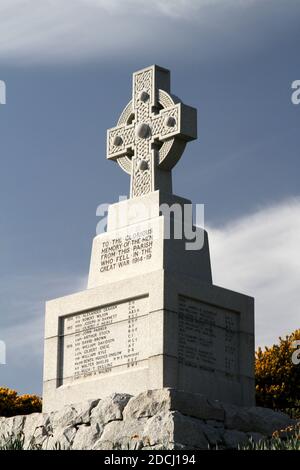 Ballantrae, South Ayrshire, Schottland, Großbritannien, Kriegsdenkmal, das Denkmal steht unter den Ruinen der Burg. Es ist ein graues keltisches Granitkreuz mit Radkopf und Bossen, die auf einem niedrigen, verjüngenden Schaft auf einem großen quadratischen Sockel liegen. Die Gedenkfeier und die Namen der Toten sind in Bleischrift auf den Gesichtern des Sockels angebracht. Die Namen der Toten aus dem 1. Weltkrieg werden nach dem Todesjahr aufgelistet, einschließlich der Namen bis 1920. Stockfoto