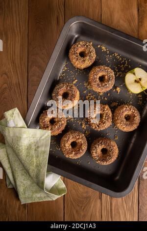 Gebackene Apfelmost-Donuts mit Apfelzutat und textiler Serviette auf Backblech auf natürlichem Holztisch. Bereit, Snack zu essen. Kleine Charge von hausgemachten Stockfoto