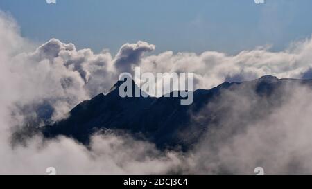 Mystischer Blick auf die Silhouetten schroffer Berge in den europäischen Alpen, umgeben von aufsteigenden Wolken über dem Montafon-Tal, Österreich im Herbst. Stockfoto