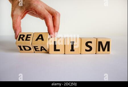 Männliche Hand dreht Würfel und ändert den Ausdruck "Idealismus" in "Realismus" oder umgekehrt. Schöner weißer Hintergrund. Geschäftskonzept. Speicherplatz kopieren. Stockfoto