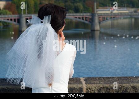 Die Braut bewundert Prag von der Karlsbrücke aus. Mädchen in einem Hochzeitskleid mit Schleier. Stockfoto