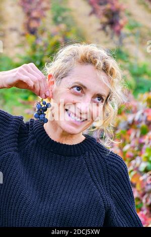 Reife junge blondy Bäuerin in einem Weinberg Ackerland scherzen mit einem Bündel von Trauben. Stockfoto