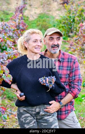 Reifes junges Paar Bauern in einem Weinberg Ackerland mit einem Bündel von Trauben. Stockfoto