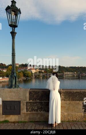 Die Braut bewundert Prag von der Karlsbrücke aus. Mädchen in einem Hochzeitskleid mit Schleier. Stockfoto