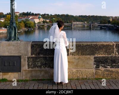 Die Braut bewundert Prag von der Karlsbrücke aus. Mädchen in einem Hochzeitskleid mit Schleier. Stockfoto