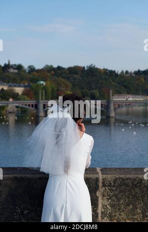 Die Braut bewundert Prag von der Karlsbrücke aus. Mädchen in einem Hochzeitskleid mit Schleier. Stockfoto