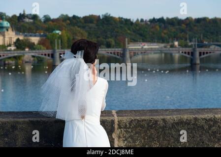 Die Braut bewundert Prag von der Karlsbrücke aus. Mädchen in einem Hochzeitskleid mit Schleier. Stockfoto