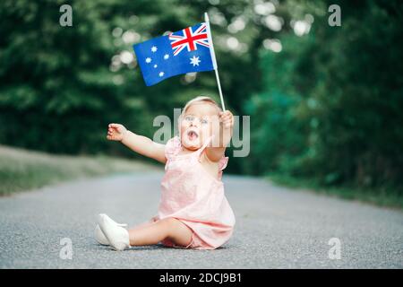 Niedlich liebenswert kaukasischen Baby Mädchen winkt australische Flagge. Lächelndes Kind, das auf der Straße im Park sitzt und den Australia Day feiert. Feiern Stockfoto