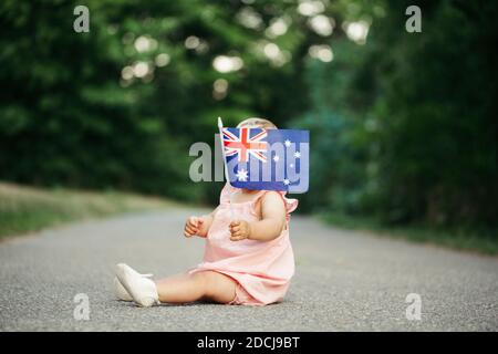 Niedlich liebenswert Baby Mädchen winken australische Flagge. Kind sitzt auf der Straße im Park mit der Australia Day Flagge. Feier der nationalen Au Stockfoto