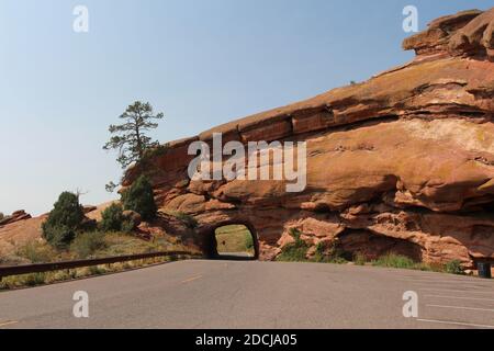 Ein Tunnel durch roten Sandstein für eine zweispurige Straße mit einem angrenzenden Parkplatz im Red Rocks State Park in Colorado, USA Stockfoto