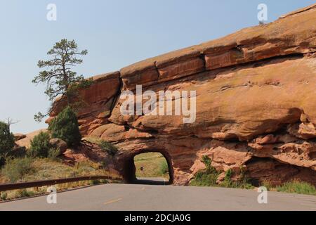 Ein Tunnel durch roten Sandstein für eine zweispurige Straße mit einem angrenzenden Parkplatz im Red Rocks State Park in Colorado, USA Stockfoto