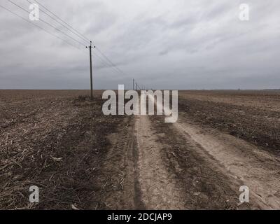 Stromleitungen entlang einer unbefestigten Straße. Düstere Abendlandschaft. Stockfoto