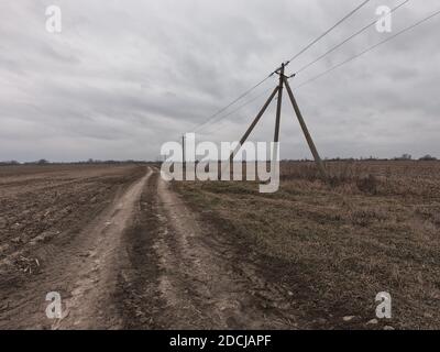 Stromleitungen entlang einer unbefestigten Straße. Düstere Abendlandschaft. Stockfoto