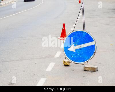 Blaues rundes Schild mit Pfeil und Verkehrskegel Stehen Sie auf der Asphaltstraße Stockfoto