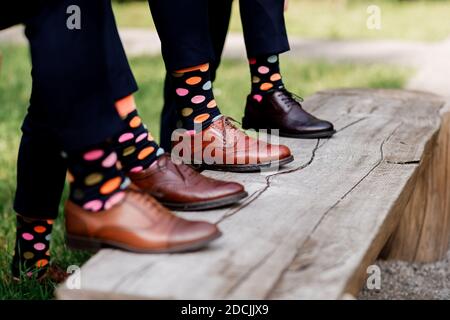 Füße des Bräutigams und Freunde des Bräutigams mit lustigen farbigen Socken. Männer in bunten Socken und schwarzen Schuhen. Sie stehen im Kreis. MODE, STYLE, BE Stockfoto