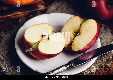 Zwei Hälften von rotem Apfel auf weißem Teller mit Vintage Messer in rustikaler Umgebung Stockfoto