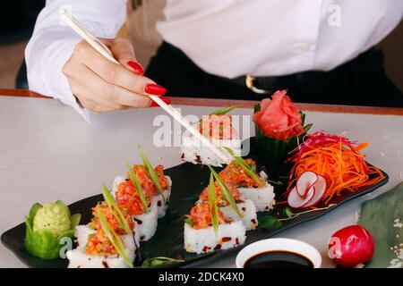 Sushi Roll auf einem schwarzen Teller, Frauenhand mit Essstäbchen, japanisches Essen Stockfoto