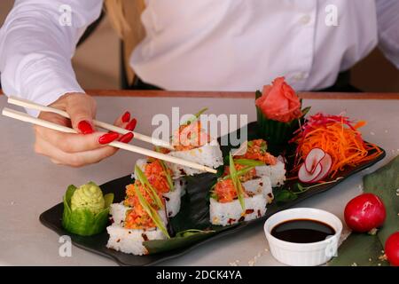 Sushi Roll auf einem schwarzen Teller mit Frau Hand halten Essstäbchen Stockfoto