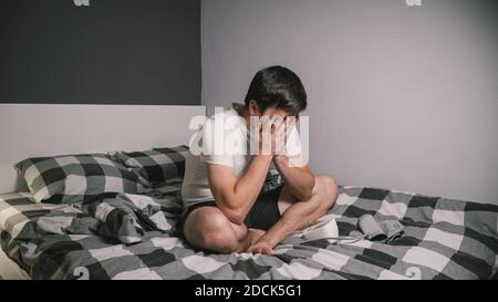 Junge kaukasische Mann misst den Blutdruck zu Hause im Schlafzimmer sitzen auf dem Bett zu Hause Kleidung. Männlich verwendet medizinische Instrument Tonometer, um seine eigenen zu überprüfen Stockfoto