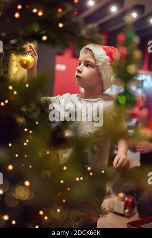 Ein kleiner Junge, der Dekorationen auf dem Weihnachtsbaum in einer Ferienatmosphäre zu Hause hängt. Gemeinsam, Neujahr, Familie, Feier Stockfoto