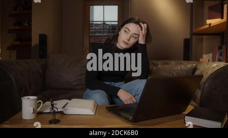 Gelangweilte Hochschule oder High School Student hübsches Mädchen, das am Tisch mit Laptop und Stiftpapier studiert, Pandemie-Fernpädagogik-Konzept Stockfoto