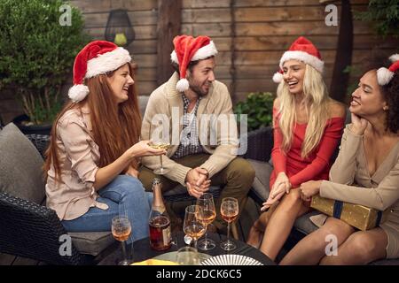 beardy Kerl flirtet mit schönen Blondine trägt rotes Kleid, santa Hüte, in der Gesellschaft von weiblichen Freunden. weihnachtszeit Stockfoto