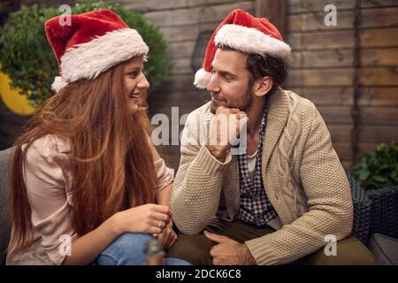 Junges erwachsenes Paar, das am Silvesterabend mit Weihnachtsmützen spricht, flirtet, lächelt. Corona, covid Konzept Stockfoto