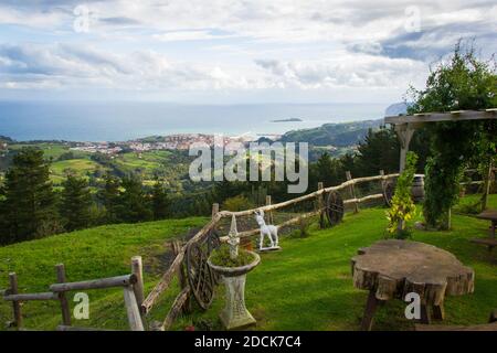 Grüne Rasendekoration mit Holzfiguren in der Nähe von Zaun und tolle Aussicht auf Bermeo Fischerdorf im Hintergrund an der Biskaya Küste, Nordspanien Stockfoto