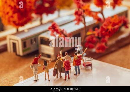 Mini-Spielzeugfiguren einer Gruppe Passanten warten oder winken an einem Zug auf einer Plattform im Herbst oder Herbst Konzept - warmen Ton Filter angewendet. Stockfoto