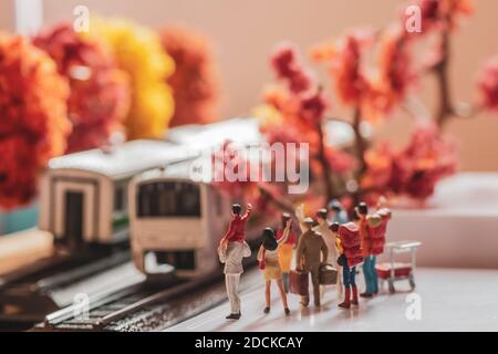 Mini-Spielzeugfiguren einer Gruppe Passanten warten oder winken an einem Zug auf einer Plattform im Herbst oder Herbst Konzept - warmen Ton Filter angewendet. Stockfoto