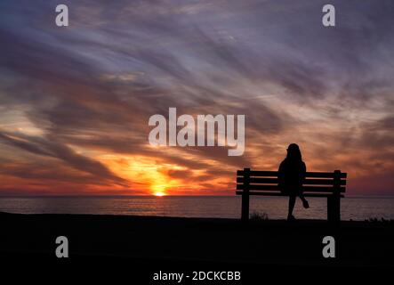 San Diego, Kalifornien, USA. November 2020. Eine Frau sitzt während des Sonnenuntergangs am Windansea Beach in La Jolla auf einer Bank. Mit COVID-19 Infektionen in ganz Kalifornien, Gov. Gavin Newsom gab eine nächtliche Ausgangssperre heraus, die "unwesentliche" Tätigkeiten und Versammlungen zwischen 10 P.M. und 5 A.M. Verbot.Kredit: K.C. Alfred/ZUMA Wire/Alamy Live News Stockfoto