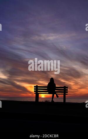 San Diego, Kalifornien, USA. November 2020. Eine Frau sitzt während des Sonnenuntergangs am Windansea Beach in La Jolla auf einer Bank. Mit COVID-19 Infektionen in ganz Kalifornien, Gov. Gavin Newsom gab eine nächtliche Ausgangssperre aus, die "unwesentliche" Aktivitäten und Versammlungen zwischen 10 Uhr und 5 Uhr Verbot.Kredit: K.C. Alfred/ZUMA Wire/Alamy Live News Stockfoto