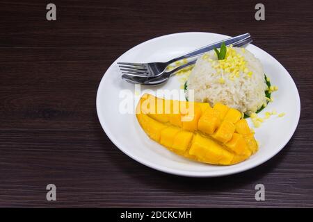 Klebriger Reis mit frischer reifer Mango mit Kokosmilch auf einem braunen dunklen Holztisch ist ein tropisches Dessert. Stockfoto