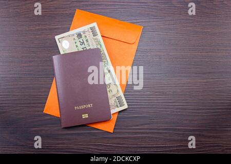 Internationaler Reisepass und japanische Banknoten auf orangefarbenem Umschlag am Tisch braun dunkles Holz. Draufsicht Stockfoto
