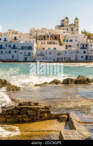 Blick auf den traditionellen Hafen von Naousa auf der Insel Paros, Griechenland, mit Meereswellen und weiß getünchten Häusern mit der christlichen Kirche von kimisis Theoto Stockfoto