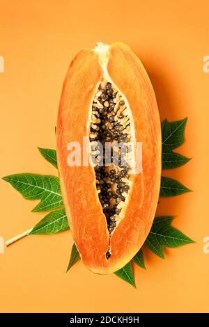 Reife frisch geschnittene Papaya-Frucht mit grünem Blatt auf orangefarbenem Hintergrund, flaches Lay, Kopierraum Stockfoto