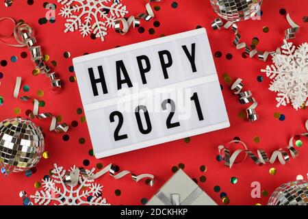 lightbox mit Wörtern Happy 2021, Geschenkbox, Disco Bälle, Schneeflocken und Urlaub Konfetti auf rotem Hintergrund. Draufsicht. Frohes neues Jahr 2021 Konzept. Stockfoto